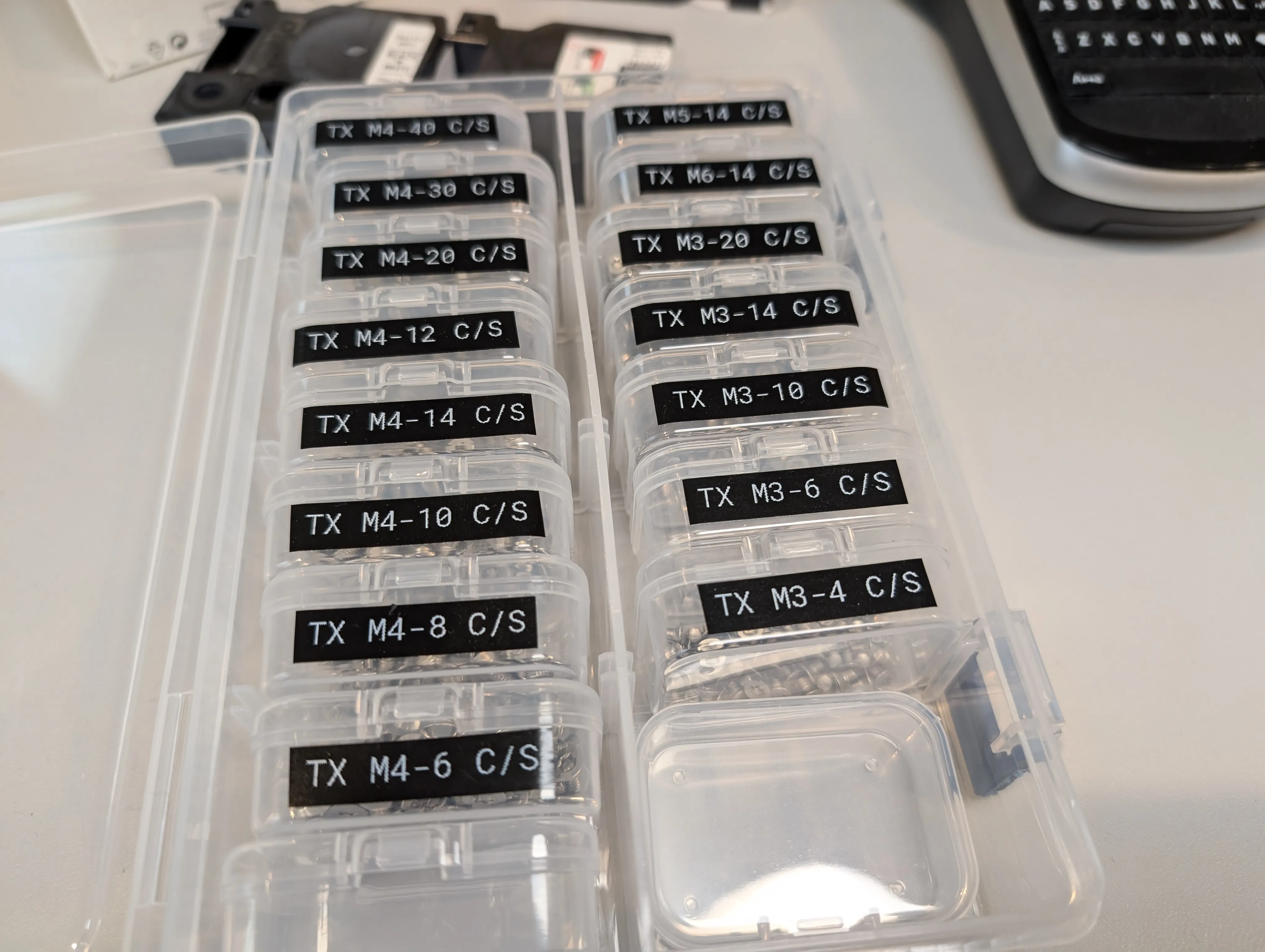 Small containers of metric screws, each labeled with their specifications in high contrast white-on-black text